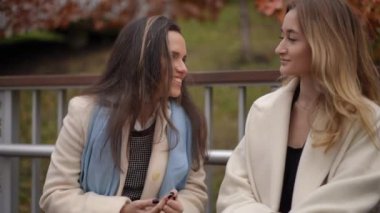 İki genç kadın, güzel bir sonbahar ortamında dışarıda neşeyle sohbet ediyor ve harika arkadaşlıklarını sergiliyorlar.