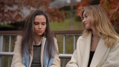 Şık paltolu bir grup kadın canlı bir sonbahar arkaplanının ortasında canlı bir sohbete girişiyor.