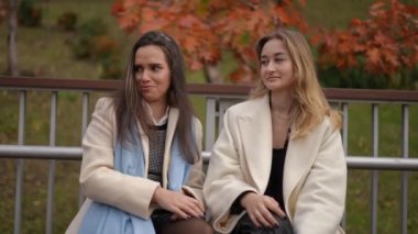 İki zarif giyinmiş kadın neşeyle ağaçların ve renkli yaprakların arasında huzurlu bir sonbahar gününün tadını çıkarıyorlar.