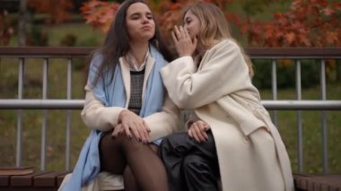 İki şık kadın neşe içinde bir kahkaha paylaşıyor. Canlı ve renkli bir sonbahar arkaplanı arasında birlikte.