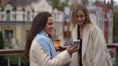 İki iyi arkadaş dışarıda güneşin altında akıllı bir telefon kullanırken neşeli ve mutlu bir anı paylaşıyorlar.