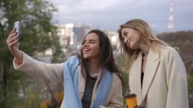 İki genç kadın mutlu bir şekilde selfie çekerken güzel bir şehir zeminine karşı birlikte eğleniyorlar.