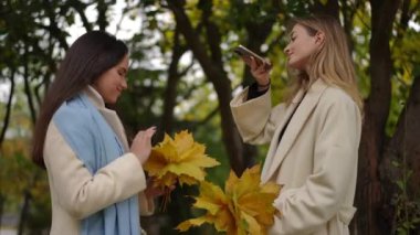 Canlı sonbahar yapraklarıyla çevrili iki yakın arkadaş, sakin bir açık havada neşeli bir şekilde değerli anıları yakalıyorlar.
