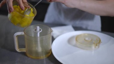 Bir el dikkatli bir şekilde meyve hazırlama sanatını gözler önüne sererek bir kaseye canlı mango küpleri ekliyor.