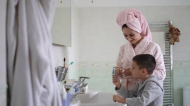 Parlak bir banyoda, şefkatli bir anne çocuğuna ağız hijyeninde yardım eder, hassas bağlarını gösterir.