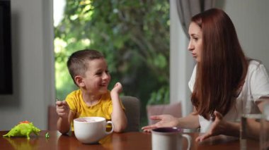 Bir anne, genç oğluyla yemek saatinde neşe içinde etkileşime geçer ve çeşitli duygular ifade eder.