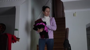 Bir kadın, sıcak ve sıcak bir evde, büyük bir demet yeni yıkanmış elbiseyi merdivenlerden yukarı dikkatle taşır.