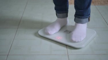 Bir insan modern dijital bir ölçekte ağırlığını evinde rahatlığında dikkatle takip eder.