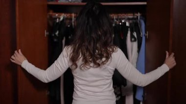 Bir kadın, önlerindeki güne hazırlanırken şık bir gardıroptan giysileri dikkatlice seçiyor.