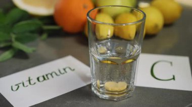 Bu, C vitamininin suda nasıl çözündüğünü gösteren görsel bir gösteri. Arka planda çeşitli meyveler var.