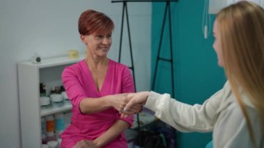 Pembe üniformalı kadın kozmetik uzmanı yeni müşterisini el sıkışarak selamlıyor. Profesyonel güzellik ortamında cilt muayenesinin başlangıcında arkadaşça bir an..