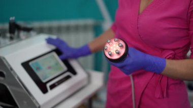 Pembe üniformalı ve eldivenli bir kadın kozmetoloji kliniğinde modern LED elektrikli süpürge masaj aleti tutuyor. Ekipmanlar aktifleştirildi ve vücut hatları oluşturulmaya ya da deri sıkılaştırma tedavisine hazır..