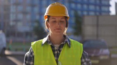 Kendine çok güvenen bir kadın inşaat işçisi gururla güvenlik kaskı ve parlak renkli bir yelek giyiyor.