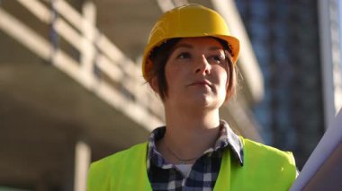 Şantiyede elinde planlar ve kahve bulunan odaklanmış bir inşaat işçisi, özveri ve profesyonelliği vurguluyor..