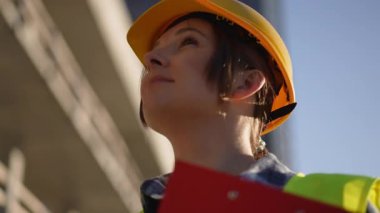 Güvenilir bir inşaat işçisi, gerekli güvenlik malzemelerini giyer, güneşli bir günde parlak mavi gökyüzüne bakar.