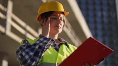 Hareketli bir şantiyede, kendini tamamen güvenlik donanımına adamış bir işçi planlarını ve planlarını dikkatle gözden geçirir.