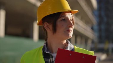 Kendine güvenen ve yetenekli bir inşaat işçisi inşaat alanında, elinde bir pano tutan, sıkı bir şapka ve güvenlik yeleği takıyor.