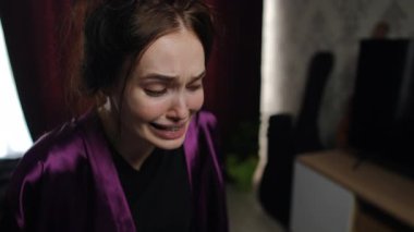 Mor saten bornozlu genç bir kadın öne doğru eğiliyor, ağlarken gözyaşları sel gibi akıyor. Onun acı dolu ifadesi ve gergin duruşu özel bir ortamda karşı konulmaz bir duygusal sıkıntı yaratıyor..