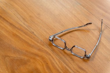 Reading glasses lie on a smooth wooden surface, bathed in natural light, suggesting a quiet moment in a comfortable indoor environment. clipart