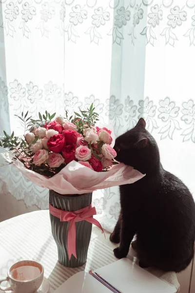 Siyah kedi gül buketini kokluyor.