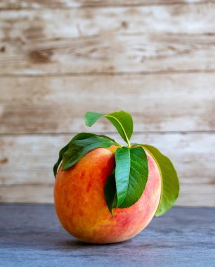 Yaprakları olan tek bir şeftali, ahşap kaplamalı bir tahta tablonun üzerinde duruyor.
