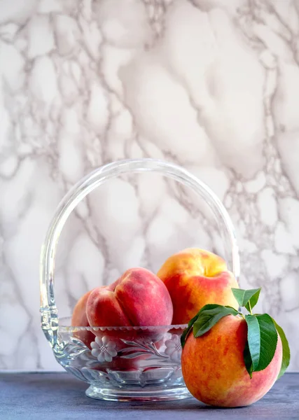 A crystal bowl of peaches rests on a slate table, with a marble background
