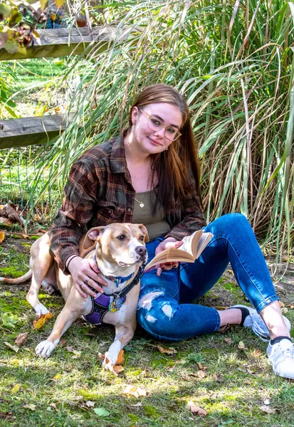 stock image Pretty young woman sits with her seizure alert dog, and reads a good book