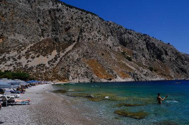 İnsanlar 1 Ağustos 2022 'de Yunanistan' ın Symi Dodecanese plajında güneş ve denizin keyfini çıkarıyorlar..