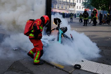 Paris, Fransa. 1 Mayıs 2023. İşçi sendikası yürüyüşü sırasında çıkan yangını söndürmeye çalışan itfaiyeciler görülüyor..