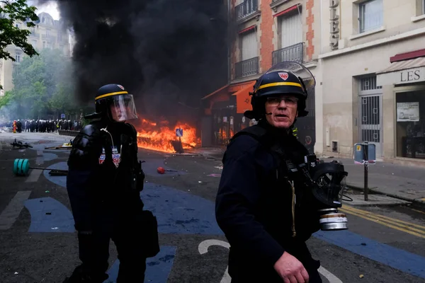 据法新社5月1日报道 法国一名防暴警察日前在法国首都巴黎的一座大楼中 在一场反对法国退休金改革法的 游行中 一名防暴警察站在一座大楼的篝火边 — 图库照片