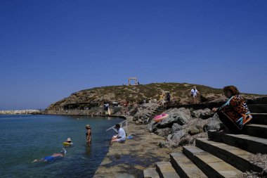 İnsanlar 10 Temmuz 2023 'te Yunanistan' ın Naxos limanında güneşlenip yüzüyorlar.