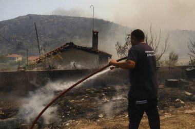 İtfaiyeciler ve gönüllüler, 22 Ağustos 2023 'te Atina' nın banliyösünde çıkan yangını söndürmek için su hortumlarını kullandılar..