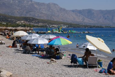 İnsanlar güneşli bir yaz gününde Yunanistan 'ın Mora kıyısındaki Agioi Theodoroi plajında güneşleniyorlar..