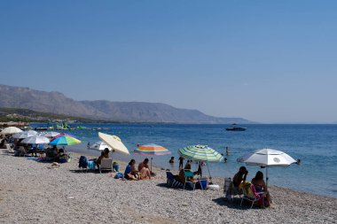 İnsanlar güneşli bir yaz gününde Yunanistan 'ın Mora kıyısındaki Agioi Theodoroi plajında güneşleniyorlar..