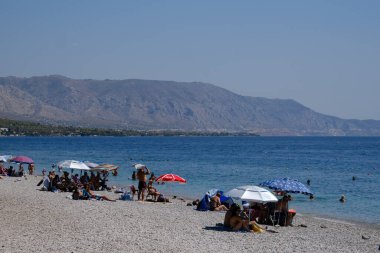 İnsanlar güneşli bir yaz gününde Yunanistan 'ın Mora kıyısındaki Agioi Theodoroi plajında güneşleniyorlar..