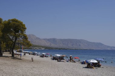 İnsanlar güneşli bir yaz gününde Yunanistan 'ın Mora kıyısındaki Agioi Theodoroi plajında güneşleniyorlar..