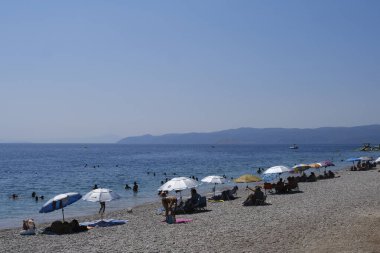 İnsanlar güneşli bir yaz gününde Yunanistan 'ın Mora kıyısındaki Agioi Theodoroi plajında güneşleniyorlar..