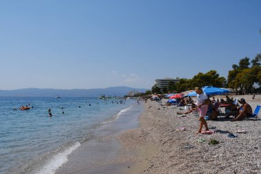 İnsanlar güneşli bir yaz gününde Yunanistan 'ın Mora kıyısındaki Agioi Theodoroi plajında güneşleniyorlar..
