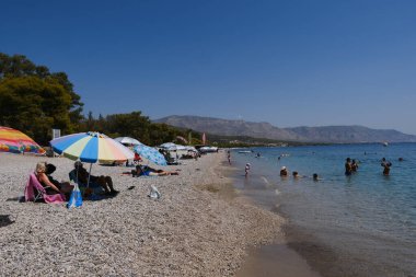 İnsanlar güneşli bir yaz gününde Yunanistan 'ın Mora kıyısındaki Agioi Theodoroi plajında güneşleniyorlar..