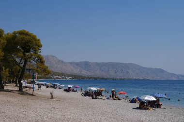 İnsanlar güneşli bir yaz gününde Yunanistan 'ın Mora kıyısındaki Agioi Theodoroi plajında güneşleniyorlar..