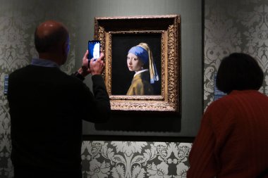 Ziyaretçiler, Johannes Vermeer 'in İnci Küpeli Ressam Kızı' nın 11 Ekim 2024 'te Lahey' deki Moritshuis Müzesi 'nde sergilediği resme bakıyorlar..