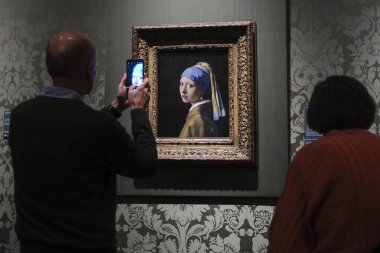 Ziyaretçiler, Johannes Vermeer 'in İnci Küpeli Ressam Kızı' nın 11 Ekim 2024 'te Lahey' deki Moritshuis Müzesi 'nde sergilediği resme bakıyorlar..