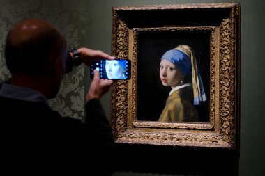 Ziyaretçiler, Johannes Vermeer 'in İnci Küpeli Ressam Kızı' nın 11 Ekim 2024 'te Lahey' deki Moritshuis Müzesi 'nde sergilediği resme bakıyorlar..