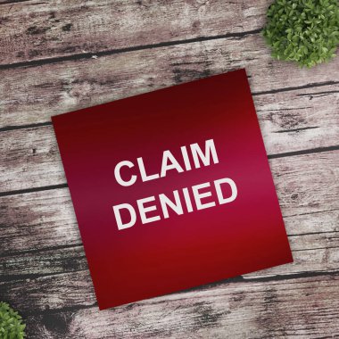 Üzerinde CLAIM DENIED yazan beyaz kart çalışma masasının üstündeki el işi zarfında modern bir dizüstü bilgisayar klavyesi ve bordo kalemle birlikte. İş yerinin düz düzeni.