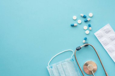 Pharmaceutical medicine tablets and stethoscope on a blue background. Face mask, surgical mask. The concept of medicine, hygiene and healthcare. Coronavirus. top view, copy space. Flu season.