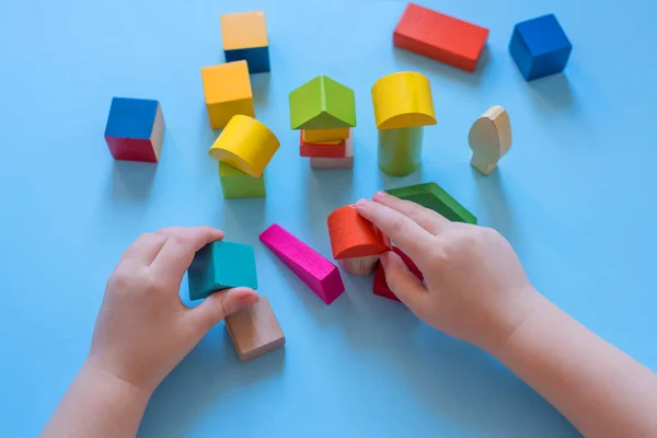 A child builds from colored cubes. Child's hands and colored wooden cubes.