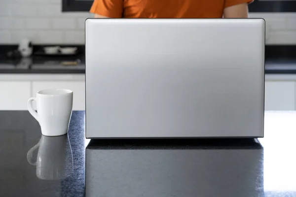 Laptop and cup of coffee on the kitchen island. Man working at home.
