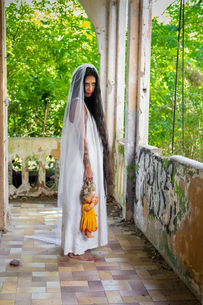 stock image Deranged bride with a doll in abandoned place. Inspired by the traditional American legend of la llorona (the weeping woman)