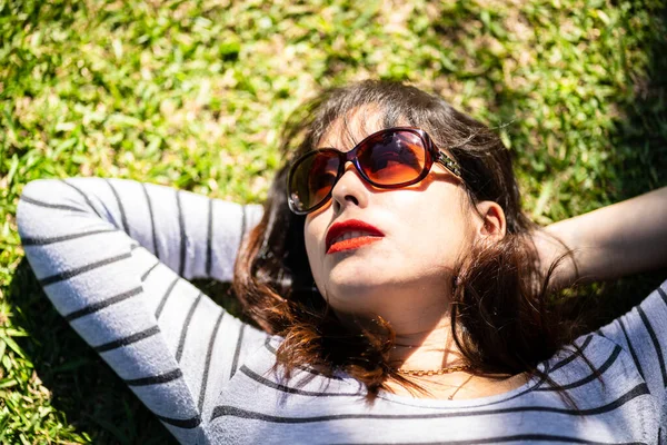 一个戴着太阳镜躺在草地上的安第斯女人的头像 灯光和阴影都被树枝过滤了 — 图库照片