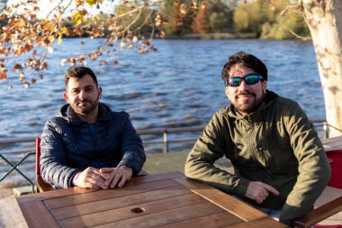 Gün batımında nehir kenarındaki bir barda oturan iki arkadaş.